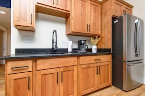 Una cocina con armarios de madera, un refrigerador de acero inoxidable, una cafetera y un lavabo con grifo.