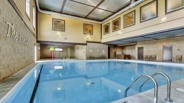 Une piscine intérieure à l’eau claire, avec un escalier en métal et un mur en pierre.