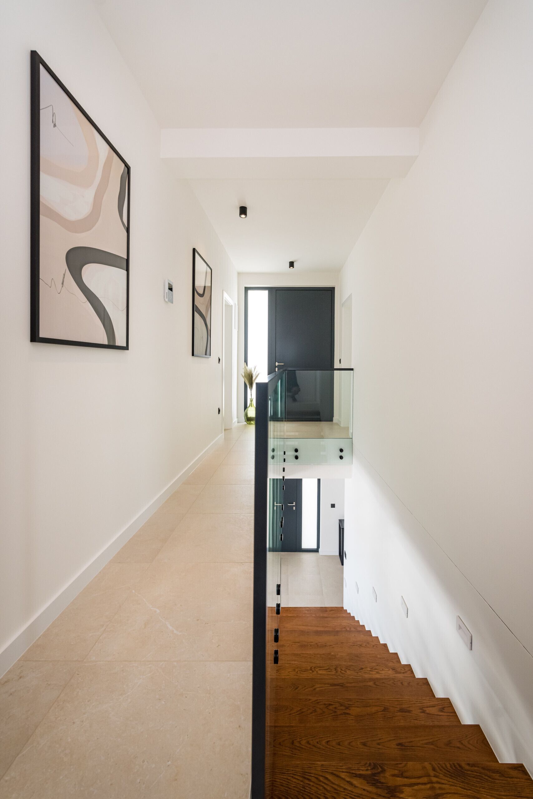 Een modern interieur met een houten trap, witte muren en abstracte kunst.