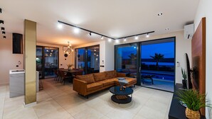 A modern living room with a brown leather sofa, a round coffee table, and a dining area with chairs and a table. - Seaview villa S. with pool (Posedarje)