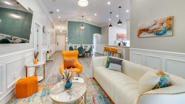 A spacious living area with a white sofa, an orange armchair, and a coffee table. There is a colorful rug on the floor, and a painting is on the wall. - Heated Pool: Davenport Home w/ Xbox & Racing Games (Davenport)
