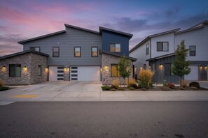 Une maison moderne à deux étages, dotée d’un garage, d’une façade en pierre et d’un jardin paysager à l’avant.