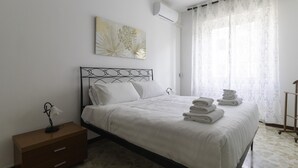 A neatly made bed with white linens and pillows, a bedside table with a lamp, and a wall-mounted air conditioner. - Italianway - Martinetti 21 B (Milan)