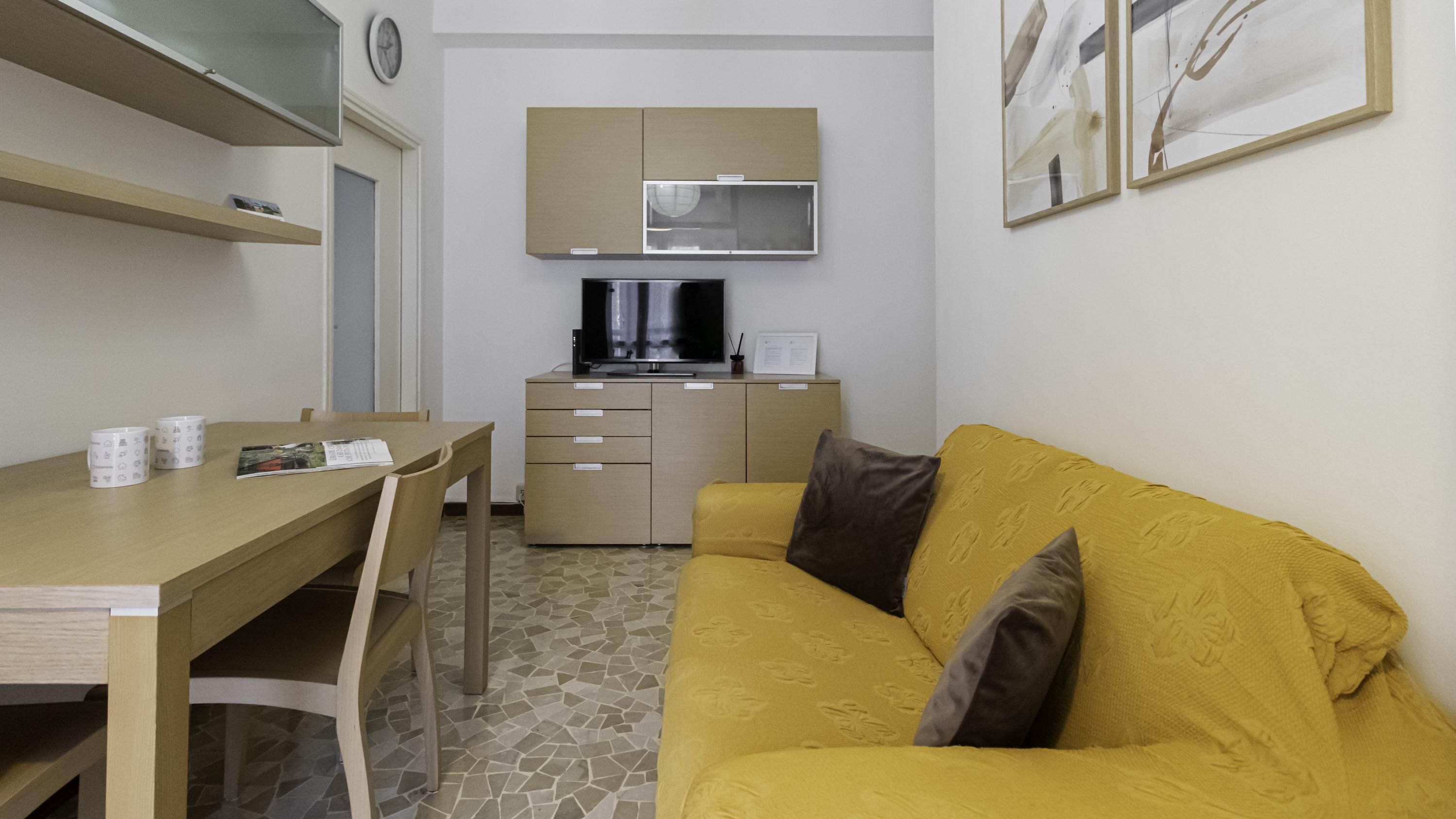 A compact living space with a dining area, a sofa, a kitchen with a microwave, and a clock on the wall.