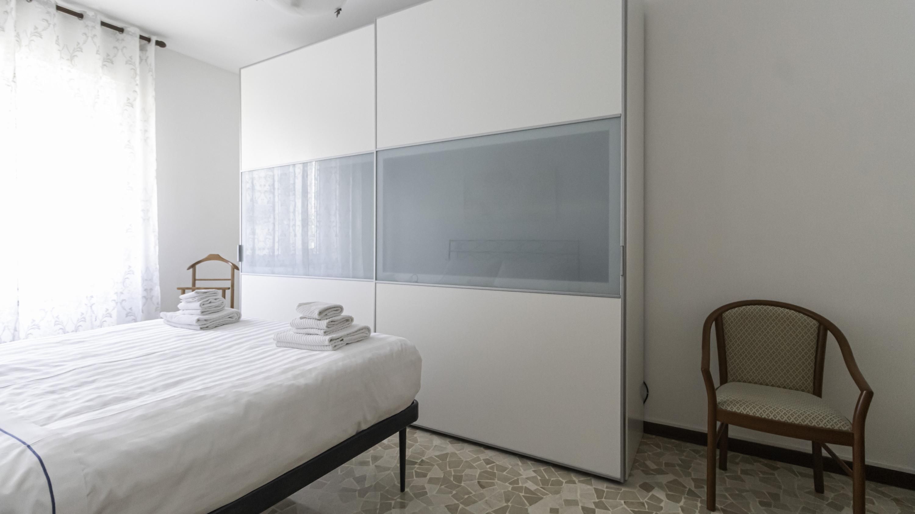 Een slaapkamer met een bed, een stoel, een kledingkast en een raam met gordijnen.