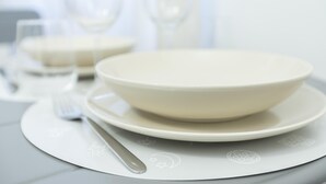 A table set with a white bowl, plate, and fork on a white placemat with a subtle design. - Italianway Comfort - Merlo 1 F (Milan)