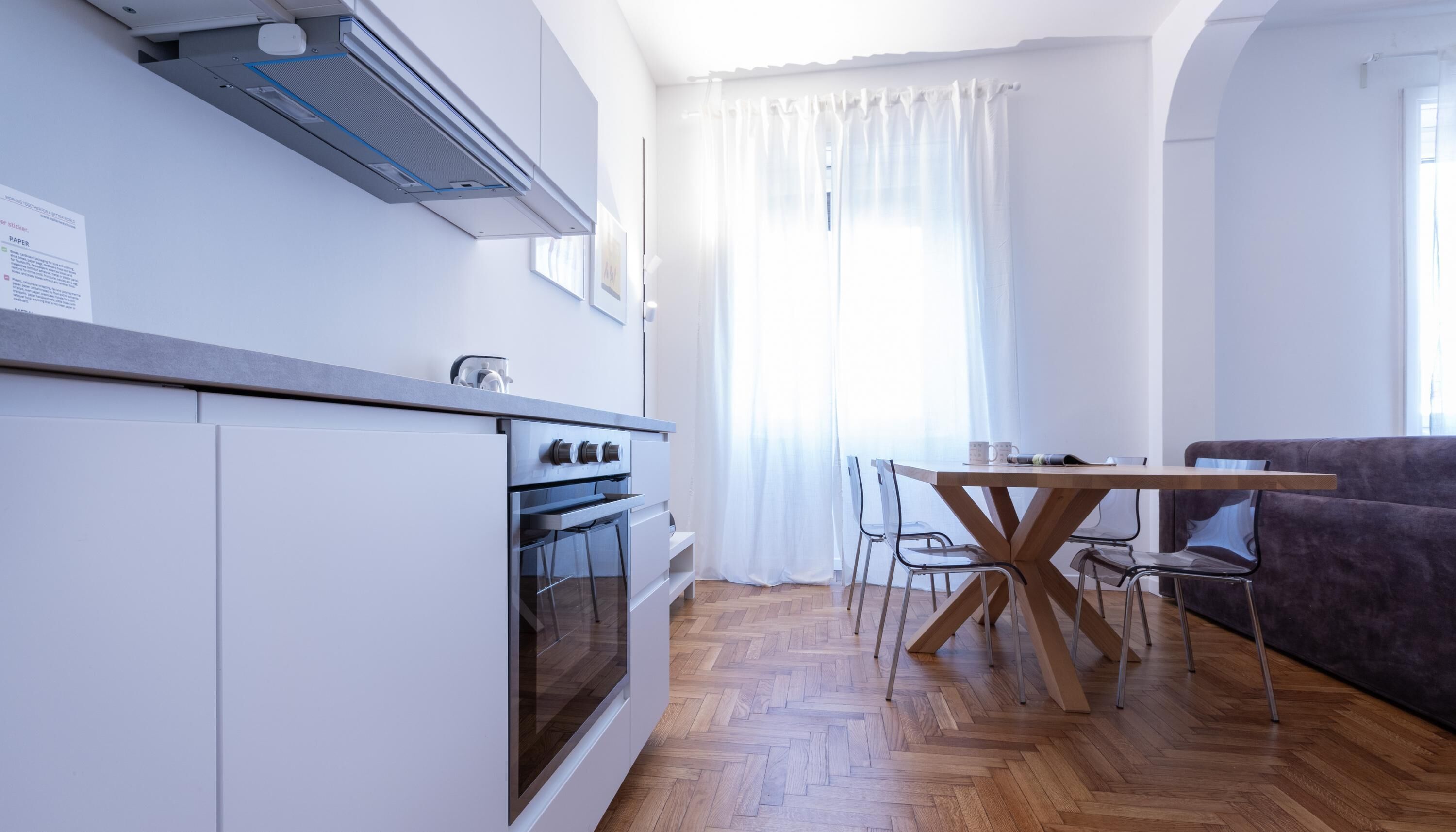 Une cuisine moderne avec des meubles blancs, un four encastré et un coin repas comprenant une table et des chaises en bois.