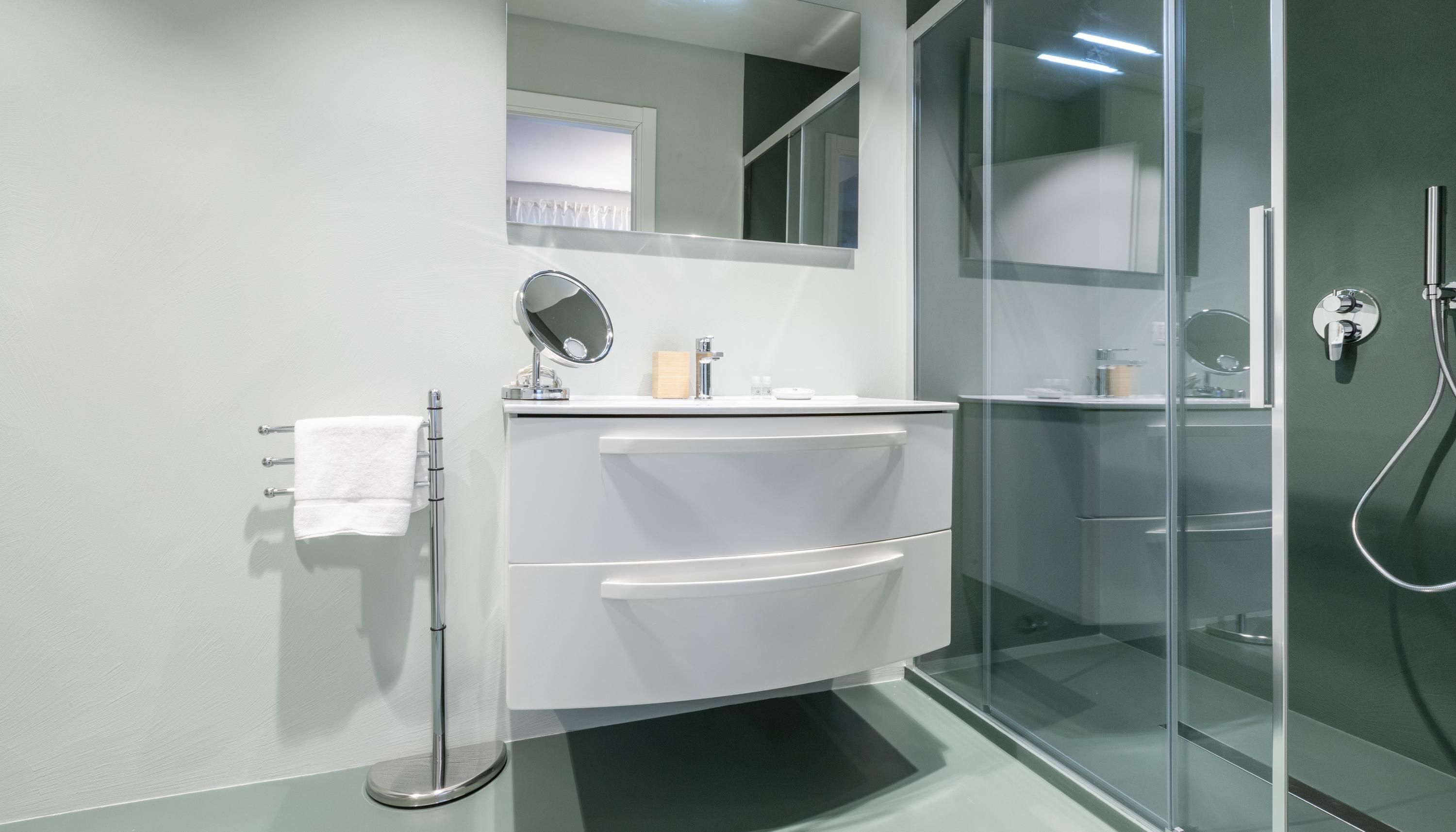 A modern bathroom with a white vanity, a round mirror, and a glass shower enclosure.
