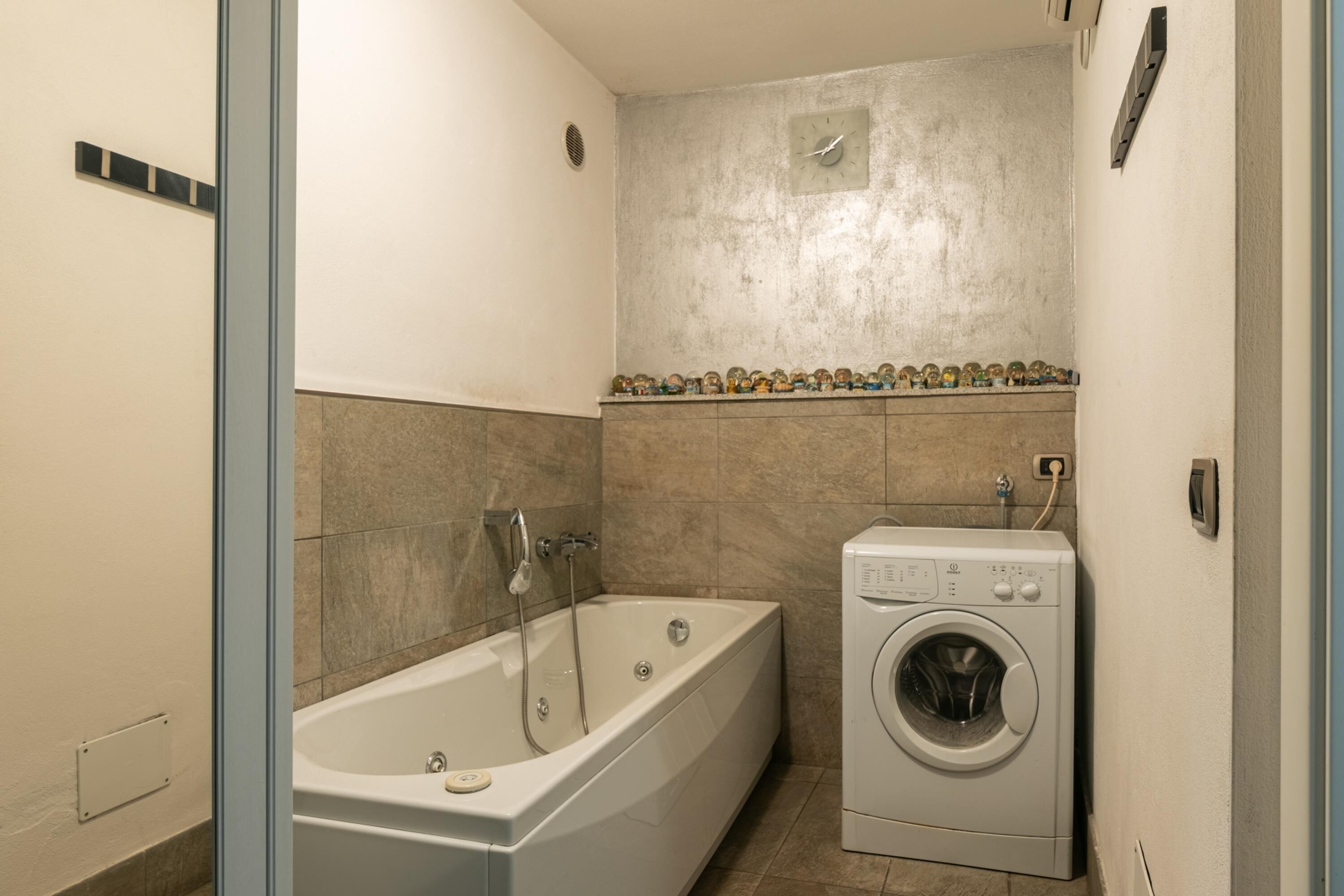 A bathroom with a bathtub, a washing machine, and a tiled wall with a decorative border.