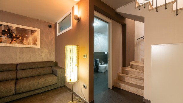 A modern living room with a sofa, a floor lamp, and a staircase leading to a bathroom. - Franciacorta Family Friendly (Adro)