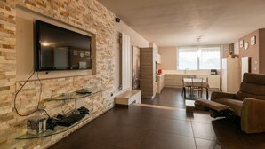 A modern living room with a flat-screen TV mounted on a brick wall, a glass coffee table, and a reclining chair. - Franciacorta Family Friendly (Adro)