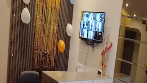 Uma área de recepção com balcão de mármore, televisão na parede e uma cortina decorativa.
