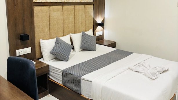 Quarto de hotel com uma cama grande, uma escrivaninha de madeira, cabeceira moderna e parede com padrão de mármore.