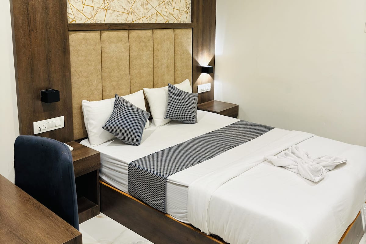A hotel room with a large bed, a wooden desk, a modern headboard, and a marble-patterned wall.
