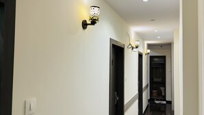 Um corredor com uma porta preta, um aplique de luz e uma ventilação.