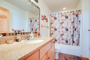 Une salle de bain avec un comptoir en granit, des meubles en bois, un lavabo blanc et des toilettes.