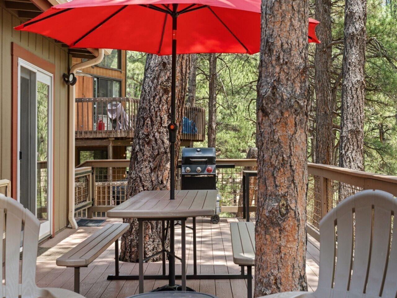 An outdoor deck with a table and chairs, a grill, and a red umbrella.