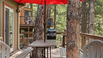 An outdoor deck with a table and chairs, a grill, and a red umbrella.