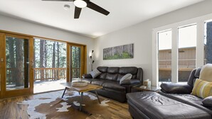 A spacious living room with a leather sofa, a glass door leading to a deck, and a large wooden floor. - Kachina Canyon Overlook Cabin (Kachina Village)