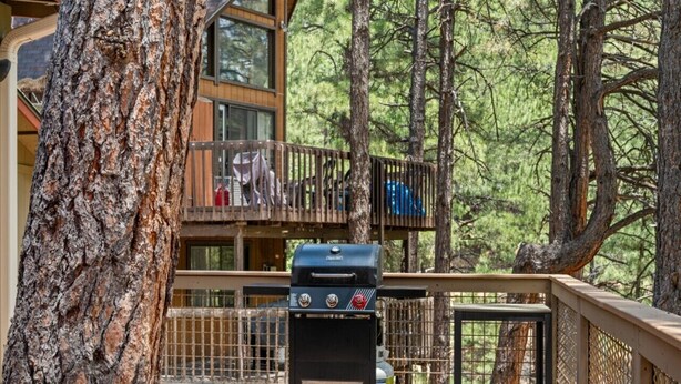 A deck with a grill, surrounded by trees and a building with balconies. - Kachina Canyon Overlook Cabin (Kachina Village)