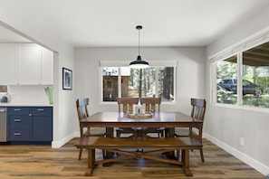A dining area with a wooden table, chairs, a pendant light, and a window with a view of trees and a car.