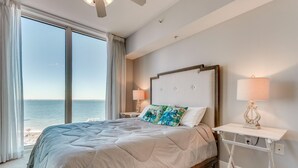 Une chambre avec un grand lit, une table de chevet avec une lampe et une vue sur l’océan.