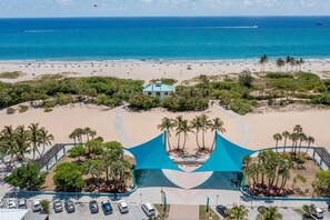 An aerial view of a beach resort with a parking area, palm trees, and a view of the ocean.