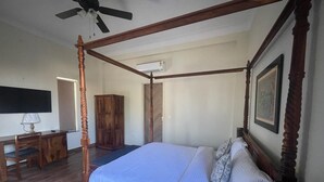 Un lit à baldaquin avec un cadre en bois et un couvre-lit blanc, un bureau avec une lampe et une armoire dans une chambre.