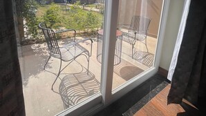 Un balcon avec des chaises en métal et une petite table, donnant sur un jardin et des immeubles.