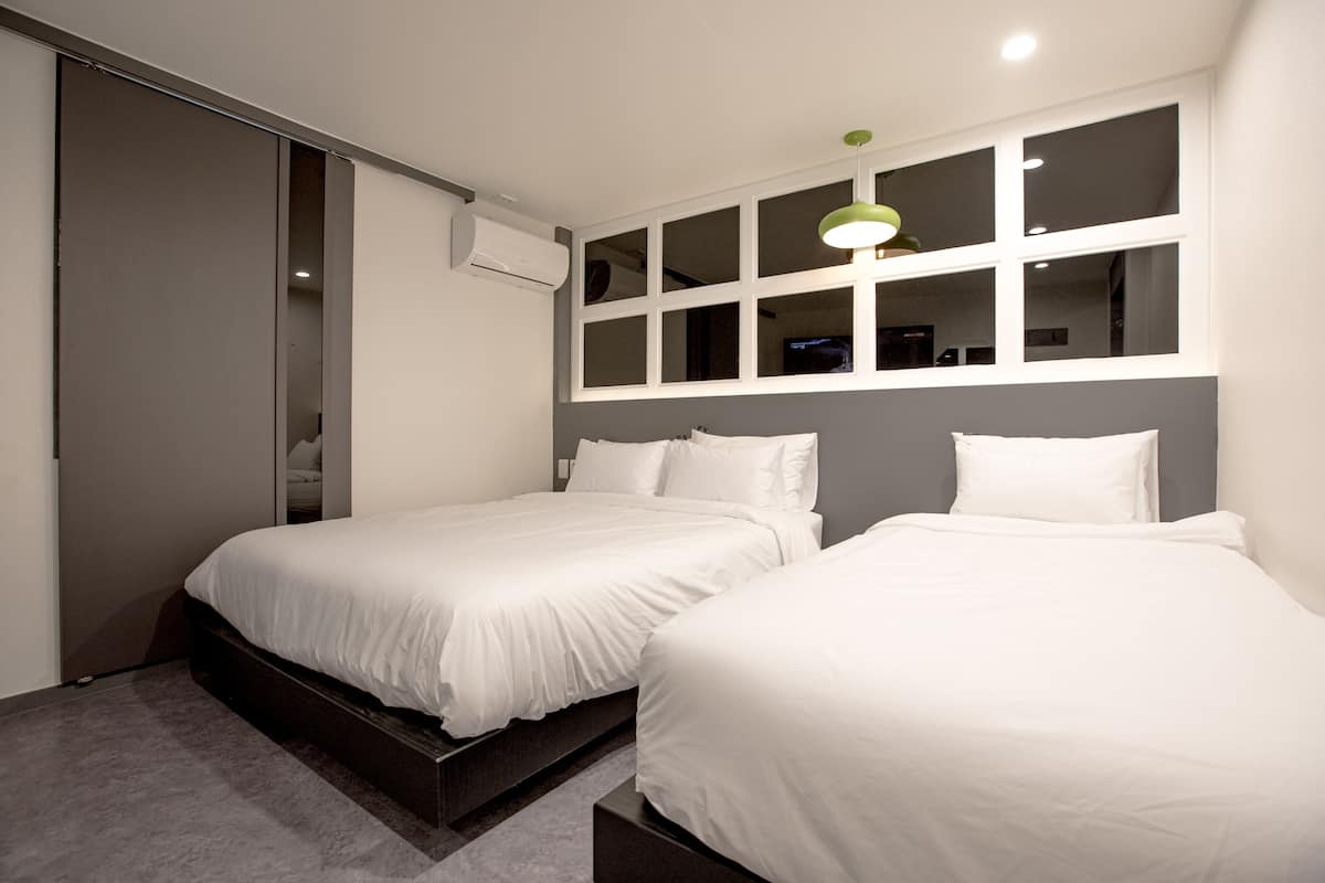 A modern bedroom with two single beds, a large window with multiple panes, and a ceiling-mounted air conditioning unit.