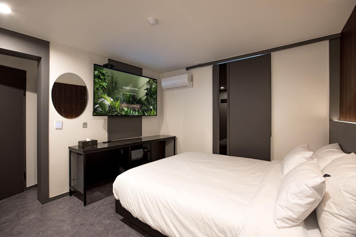A modern hotel room with a large bed, a flat-screen TV mounted on the wall, a dark wooden desk, and a sliding door closet.