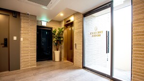 Un moderno vestíbulo de hotel con pared de ladrillo, una planta en maceta, un ascensor y una puerta de cristal con un cartel.