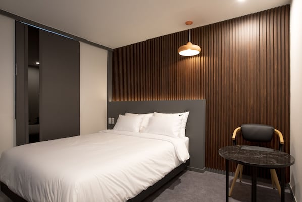 Un dormitorio moderno con una cama, una mesita redonda y una silla.