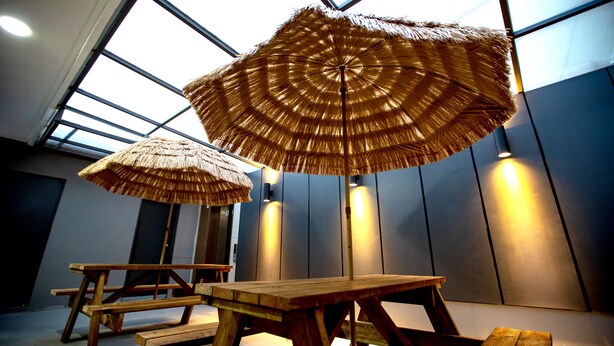Una habitación con un ventanal grande, una mesa de madera y un paraguas de paja.