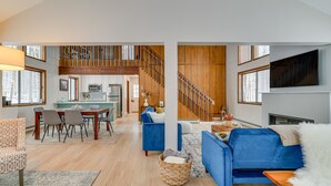 A spacious living area with a dining table, blue sofas, and a staircase leading to an upper level. - Family-Friendly Big Bass Lake Vacation Rental! (Covington Township)