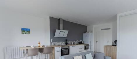 A modern kitchen with a central island, a dining area with bar stools, and a grey sofa with a decorative pillow.