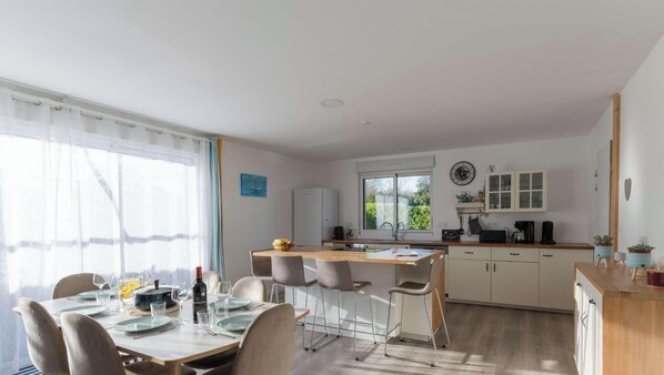 A modern kitchen with white cabinets, a dining area with a table set for four, and a large window providing natural light. - Roscaroc Enez Hir - Charming T4 near to the beach (Ploudalmézeau)