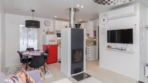 A modern living room with a sofa, a fireplace, a dining area with a table and chairs, and a kitchen in the background. - Hillaniitty by Interhome (Kuusamo)