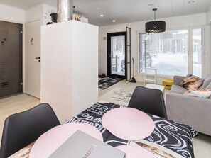 A modern living room with a sofa, a dining table with chairs, and a large window with blinds.