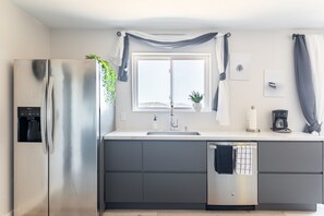 Eine moderne Küche mit einem Edelstahl-Kühlschrank, einem Geschirrspüler, einer Spüle und einem Fenster mit Vorhängen.