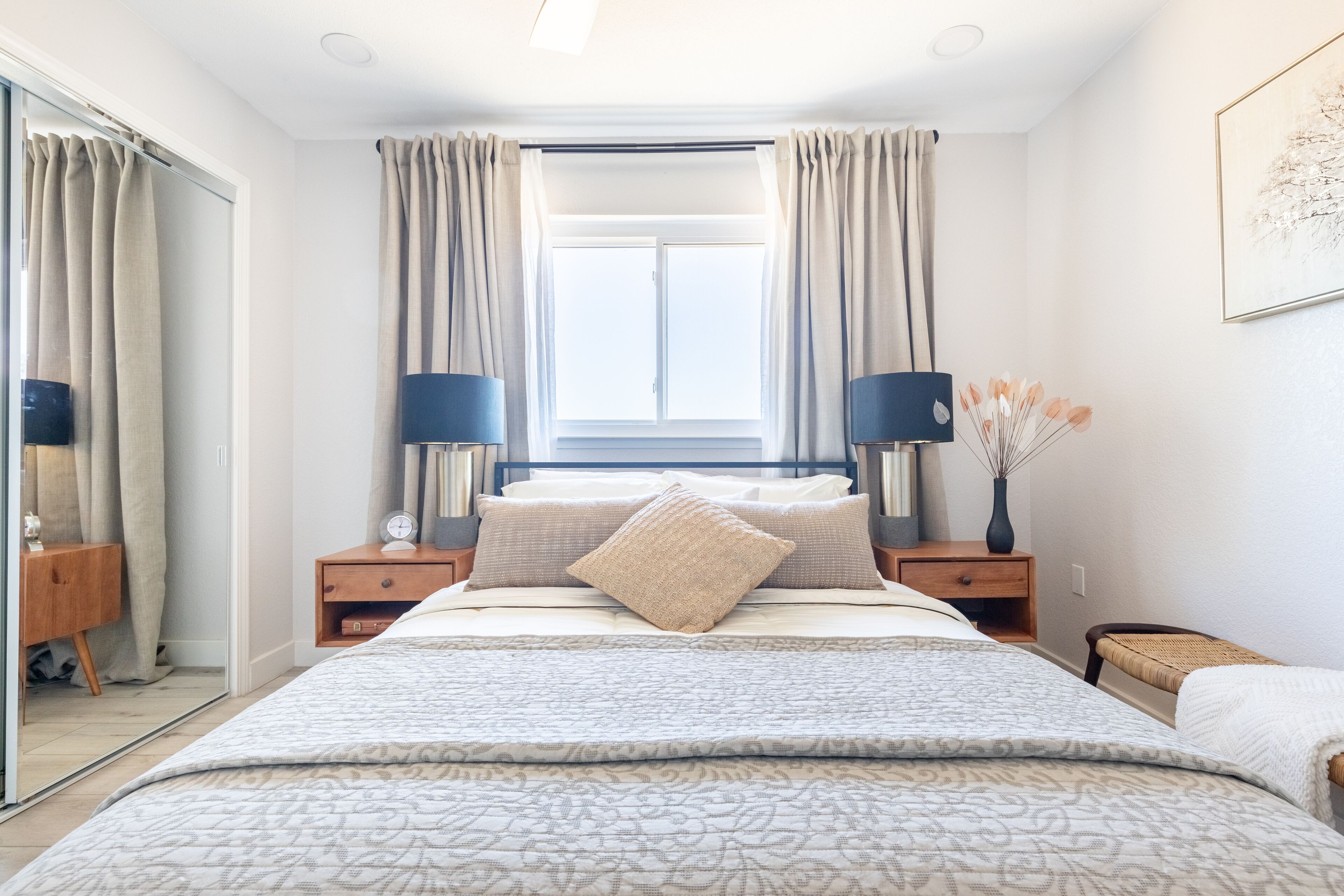 Een moderne slaapkamer met een groot bed, twee nachtkastjes met lampen, een bijzettafeltje en een spiegel.