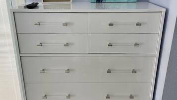 A white chest of drawers with multiple drawers, a remote control, and a framed artwork on top.