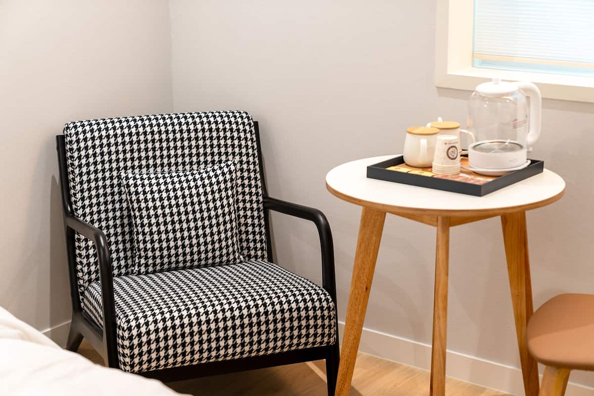 A houndstooth patterned chair next to a small round table with a coffee pot and cups.