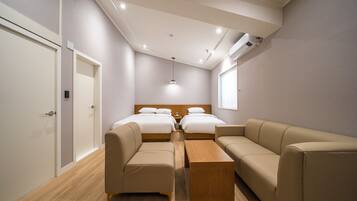 A modern hotel room with two beds, a sofa, a wooden coffee table, and an air conditioning unit on the wall.