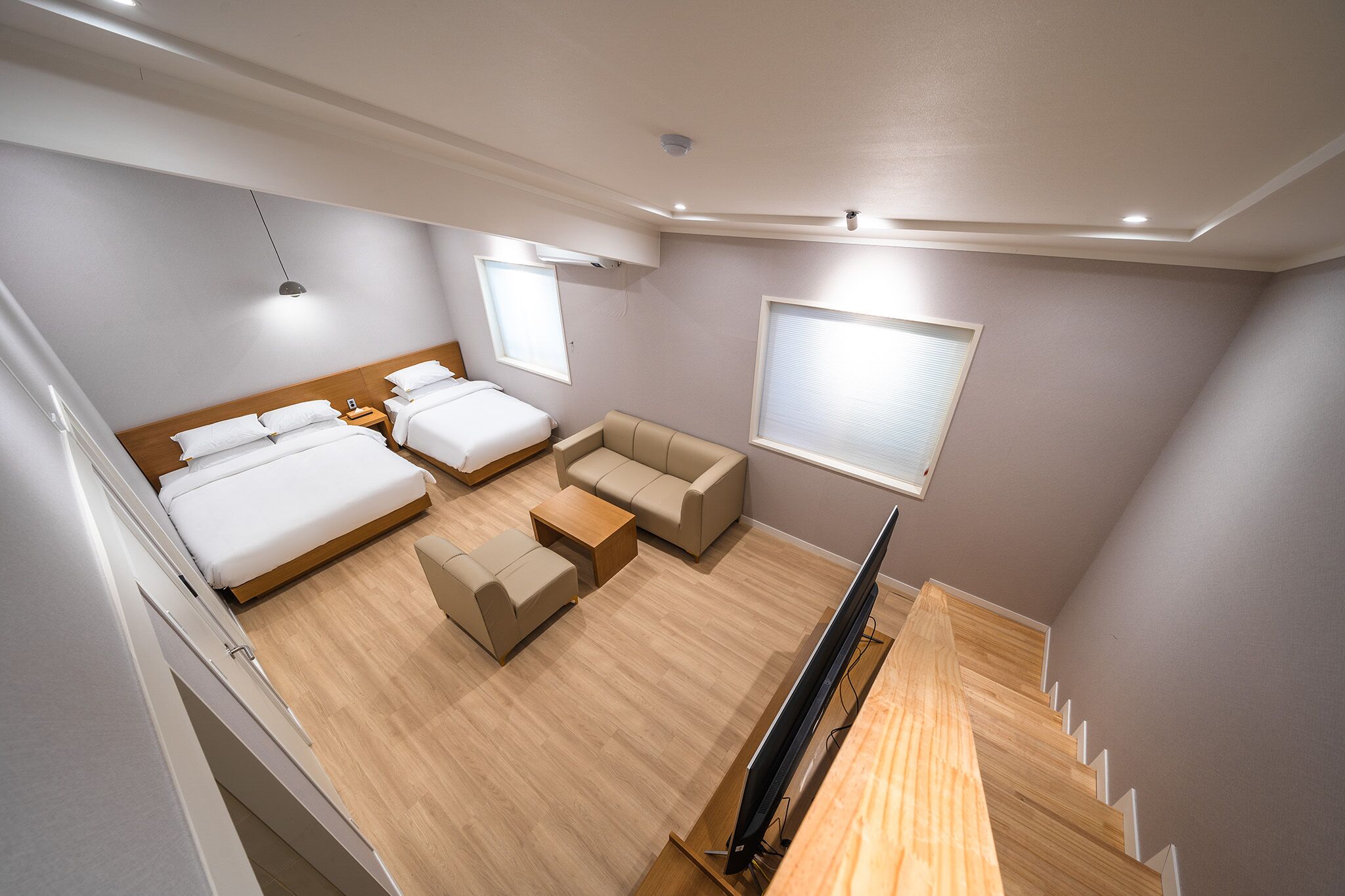 A modern hotel room with a large bed, a sofa, a coffee table, and a TV.