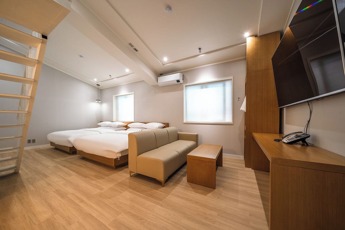 A modern bedroom with a bed, sofa, desk, and a TV.