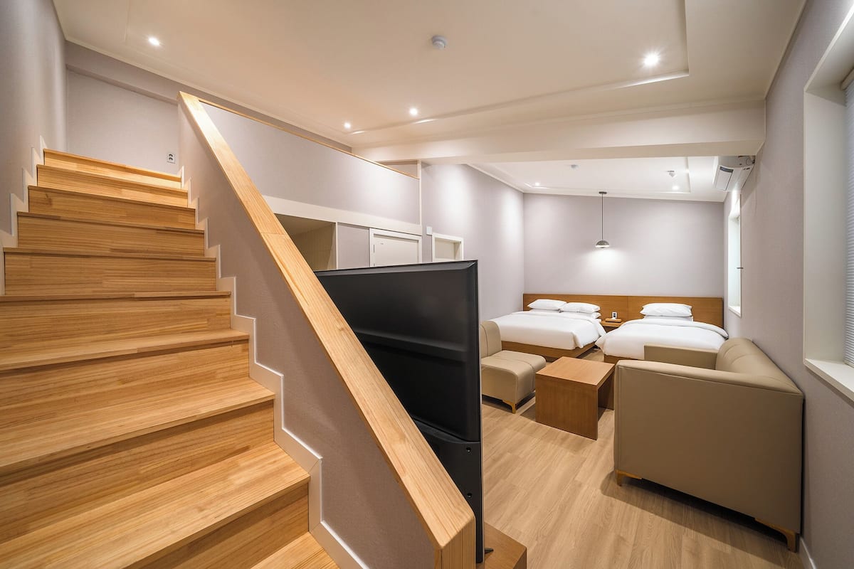 A hotel room with a wooden staircase, a bed, a sofa, and a TV.