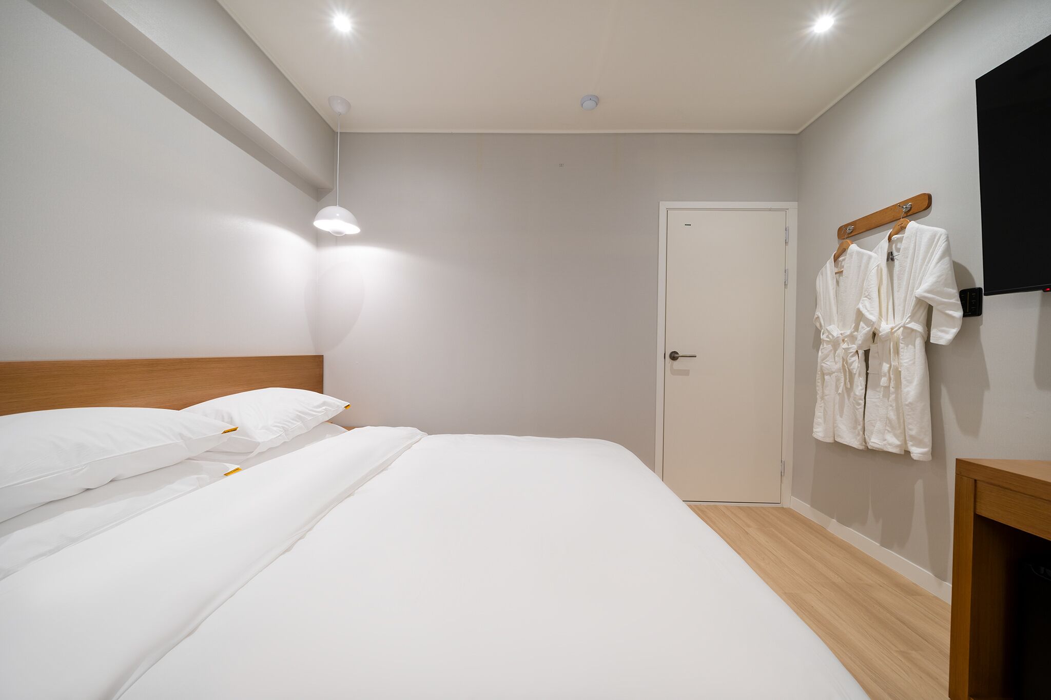 A hotel room with a neatly made bed, a wooden headboard, a door, and a wall-mounted TV.