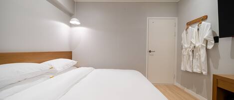 A hotel room with a neatly made bed, a wooden headboard, a door, and a wall-mounted TV.