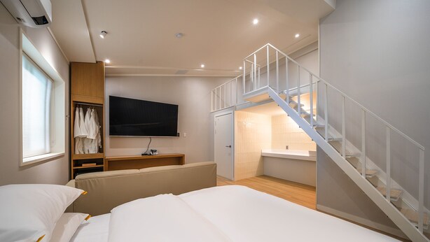 A modern bedroom with a bed, a TV, a wardrobe, and a staircase leading to a bathroom. - Mono Hotel (Suwon)